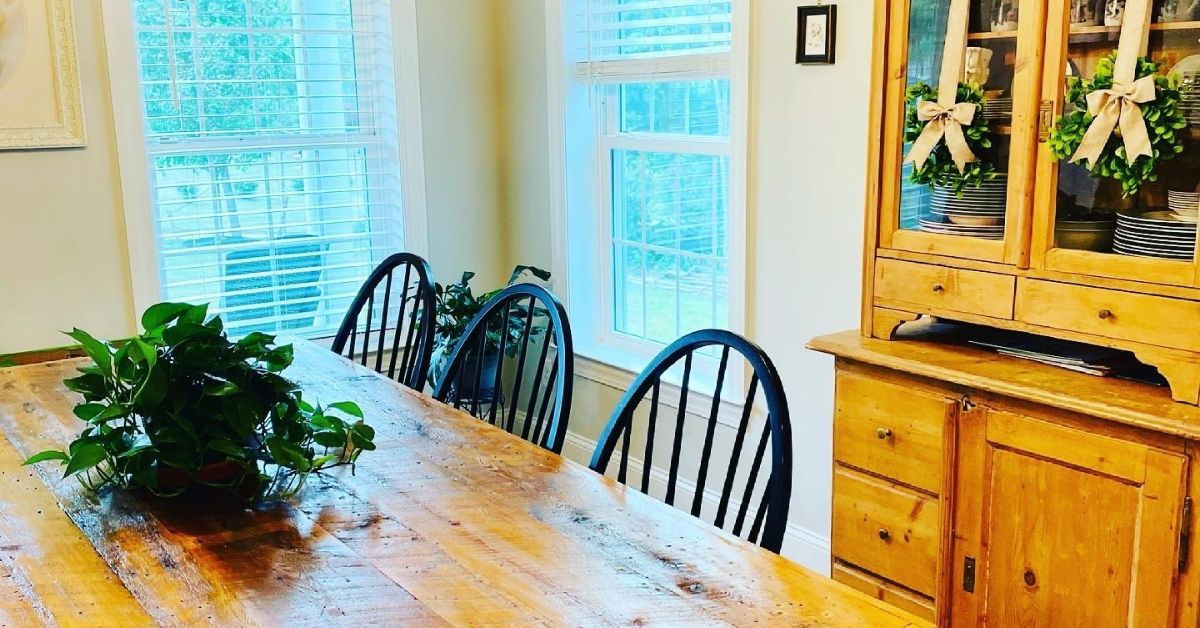 Farmhouse table with a real plant centerpiece and wood antique hutch with faux plant wreaths